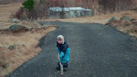Young-boy-play-fighting-with-a-long-stick-on-a-gravel-road-out-in-the-country