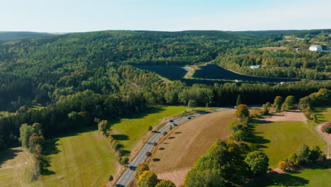 Aerial-Ascending-Along-Winding-German-Highway-with-Cars-Traffic-Through-Forests-in-Countryside-and-Large-Solar-Panel-Farm-Field-on-a-Hill