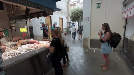 Una-Mujer-Bebe-Su-Bebida-Mientras-Observa-El-Animado-Mercado-De-Pescado-En-Las-Calles-De-Sevilla,-España.