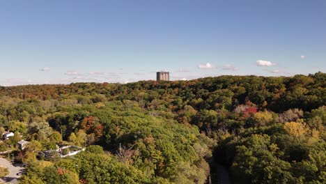 Drone-flying-over-forest-of-trees-and-looking-towards-escarpment-with-building-in-background