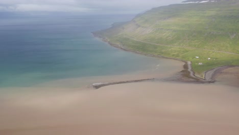 Aerial-view-of-river-delta-with-blue-and-brown-water-of-sea-during-foggy-day---Green-Iceland-Island-in-background