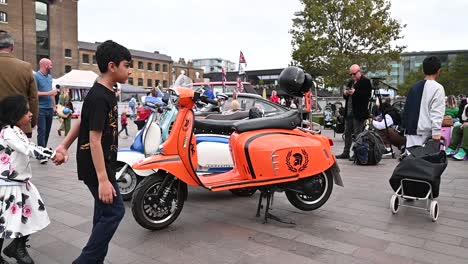 Childrebn-walking-past-an-orange-Vespa,-London,-United-Kingdom