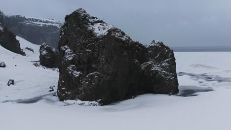 Aerial-view-rising-over-a-rock,-approaching-the-sea,-gloomy,-winter-evening-in-Iceland