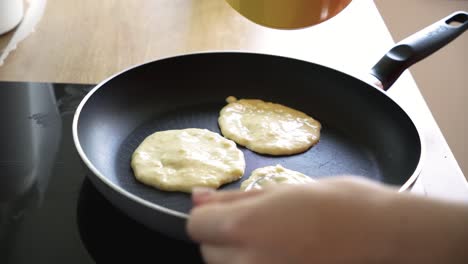 Closeup-of-female-hands-making-pancakes-on-a-hot-black-pan-on-electric-stove