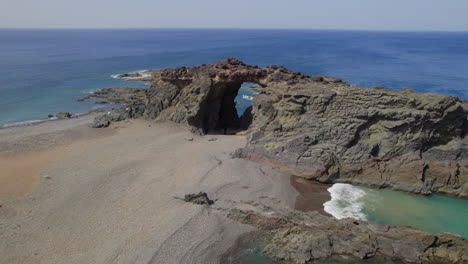 Fuerteventura-Island:-aerial-view-traveling-out-to-the-Jurado-arch-and-the-beach-on-a-sunny-day-with-beautiful-colors