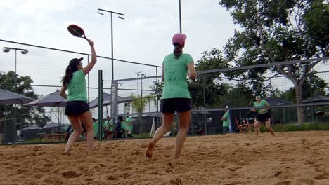 women-playing-ball-in-padel-match,-winning-a-point,-smashing-and-jumping-on-sunny-beach-padel-sandcourt