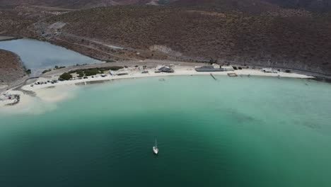 Aerial-dolly-backwards-shot-from-the-beautiful-coast-of-Baja-California-Sur-Mexico-Pichilingue-Beach-near-La-Paz-overlooking-the-wasteland-or-desert-landscape-and-the-calm-sea-with-floating-boats