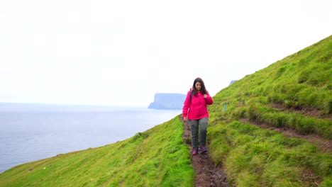 Woman-hiking-muddy-path-in-Kalsoy,-Vidoy-Island-in-background