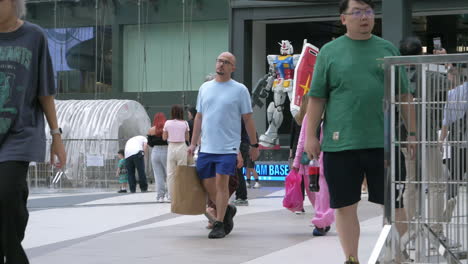 People-are-busy-walking-outside-of-Siam-Paragon-in-Bangkok-with-the-BTS-train-station-with-trains-leaving-and-stopping-for-passengers,-in-Thailand