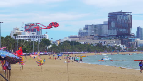 Kites-of-different-designs-and-sizes-are-tied-to-polls-to-display-how-they-fly-so-it's-easy-to-buy-and-choose-at-a-beach-with-hotels-and-condos-on-a-coastal-road-in-Pattaya,-Thailand