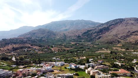 Mountain-range-and-small-town-in-Crete,-aerial-ascend-view