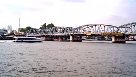 A-river-cruise-boat-passes-beneath-the-Krung-Thon-Bridge-spanning-the-Chao-Phraya-river,-a-gateway-to-major-tourist-attractions-in-Bangkok,-Thailand