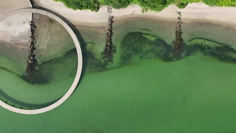 Infinity-bridge-in-Aarhus-Denmark---Aerial-above-circular-shaped-bridge-while-moving-slowly-to-the-right-and-along-the-beach