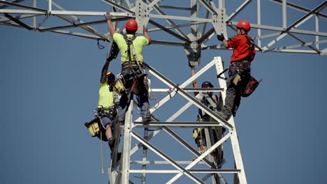 Handaufnahme-Von-Elektrikern,-Die-Mit-Schutzausrüstung-Und-Schutzhelmen-Gesichert-Sind,-Während-Sie-Gefährliche-Reparaturarbeiten-An-Stromleitungen-Durchführen,-Die-An-Einem-Strommast-In-Der-Höhe-Befestigt-Sind