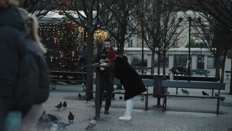 Couple-enjoys-street-food-in-Prague's-center-amidst-pigeons-during-Christmas