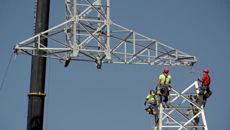 Four-workers-ready-to-fix-electric-pole-top-into-place,-heavy-crane-lifting