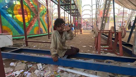 A-slum-kid-is-sitting-under-the-amusement-doing-tata-bye-bye-to-the-camera