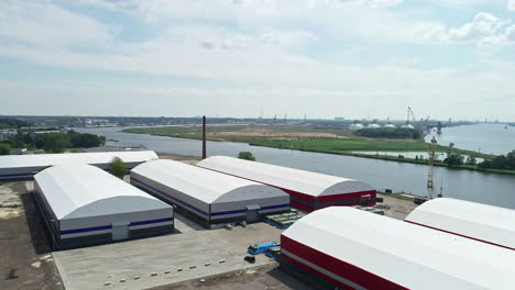 Massive-grain-storage-units-near-river-water,-aerial-drone-view