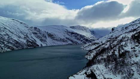 Aerial-rising-shot-of-snowy-mountains-and-calm-waters-in-the-fjords-of-Norway