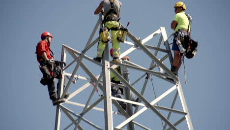 Workers-construction-high-power-line-pole,-tilt-down-view