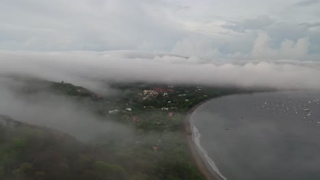 Clouds-spill-falling-down-tropical-mountains-to-Playa-Del-Coco,-Guanacaste-Region,-Costa-Rica,-aerial-panoramic-overview
