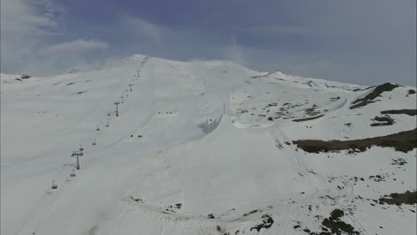 Ski-chair-lift-rises-up-along-stunning-snow-covered-mountain-in-Austria,-aerial-dolly