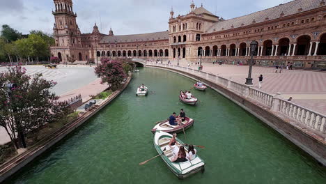 Plaza-De-Espana-Kanal-Mit-Reiseleitern,-Die-Ruderboote-Unterhalb-Der-Großen-Promenade-Und-Des-Gebäudes-Rudern