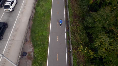 An-aerial-view-of-a-man-jogging-on-a-paved-path-next-to-the-Belt-Parkway-on-a-cloudy-day