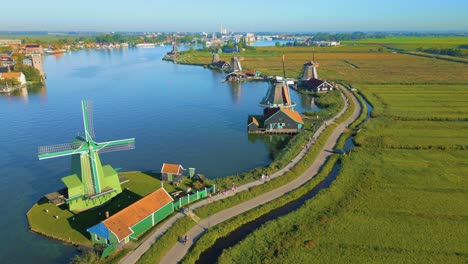 Aerial-drone-shot-of-cyclists-passing-by-a-still-windmill-in-Zaanse-Schans,-Netherlands
