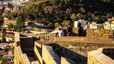 Tourists-relax-at-sunset-on-Gibralfaro-walking-path-overlooking-idyllic-sea-port-town