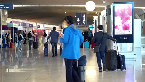 People-walking-with-suitcases-at-the-airport-with-advertising-and-information-screens,-crowded-but-uncluttered-place