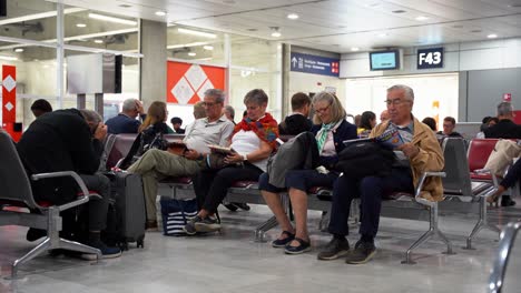 Elderly-couple-sitting-in-airport-boarding-areas-while-waiting-for-their-flight-reading,-Paris,-France