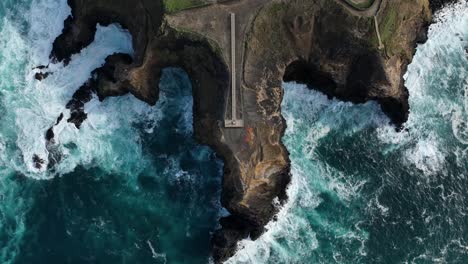 Top-down-drone-descent-over-Fenais-da-Ajuda-lighthouse-on-rugged-cliffs,-Azores