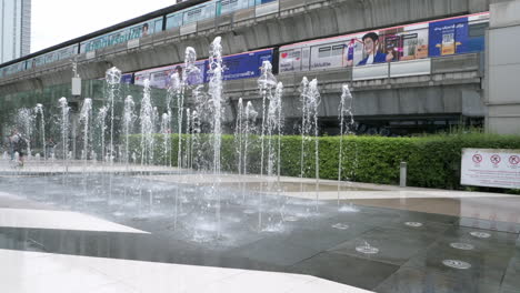 Shoppers-walking-and-taking-photos-in-front-of-a-fountain-at-a-walkway-that-connects-the-two-malls---Siam-Paragon,-Siam-Discovery,-and-the-BTS-train-station-in-Bangkok,-Thailand