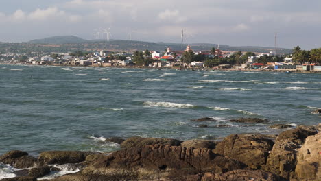 Rocky-coast-of-Mui-Ne-with-a-wind-farm-in-the-background,-Traditional-Vietnamese-town