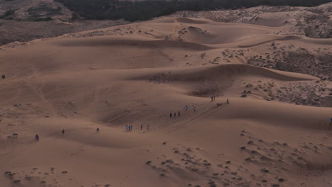 Tourists-trek-across-famous-red-sand-dunes-of-Mui-Ne,-sledding-down-and-exploring-vast-dry-landscape