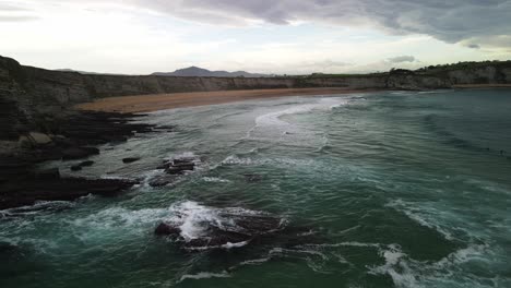 Ocean-waves-crashing-on-rocks-at-Spain-coastline-with-sand-beach-aerial