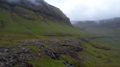 Fog-filled-lush-green-grassy-valley-in-Nordradalsskard,-exposed-volcanic-rocks-and-cliffside