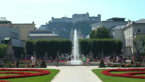 Beautiful-Gardens-of-Mirabell-Palace-with-Fountain-and-Statues-in-the-Middle-and-Fortress-Hohensalzburg-in-Background-with-People-Walking-Around