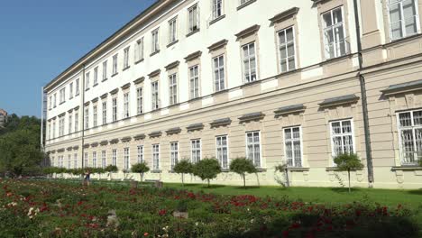 Una-Joven-Camina-Cerca-De-La-Fachada-Del-Palacio-Mirabell-Con-Jardines-En-Un-Día-Soleado