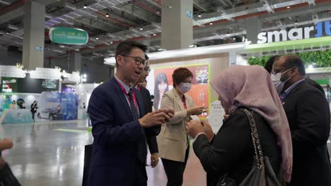 Man-smiles,-bows,-and-gives-business-card-to-woman-in-tech-summit-conference