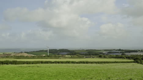 Wind-turbine-standing-in-green-fields-of-Devon,-with-blue-sky-with-clouds,-static-shot