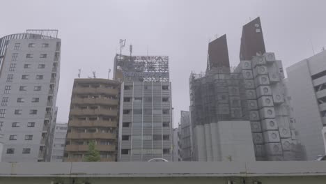 The-Nakagin-Capsule-Tower-Building-being-demolished-on-a-rainy-day-with-a-raised-highway-in-the-foreground-with-traffic-passing-by
