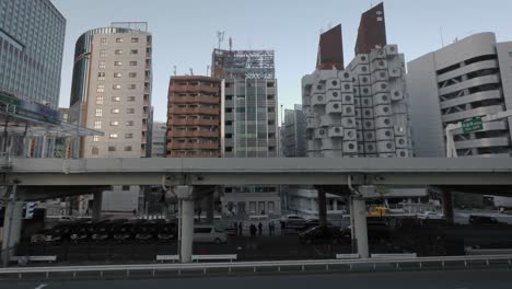 The-Nakagin-Capsule-Tower-Building-with-a-raised-highway-in-the-foreground-with-traffic-passing-by