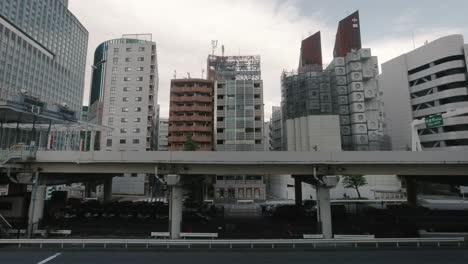 El-Edificio-De-La-Torre-Cápsula-Nakagin-Está-Siendo-Demolido-Con-Una-Carretera-Elevada-En-Primer-Plano-Con-El-Tráfico-Que-Pasa.