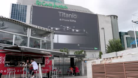 People-are-seen-at-a-coffee-shop-as-a-large-commercial-billboard-announcing-the-Apple-iPhone-15-Pro-for-sale-appears-in-the-background