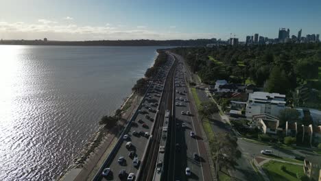 Traffic-car-along-State-Route-2-and-train-passing-at-sunset,-Swan-river-at-Perth-in-Australia