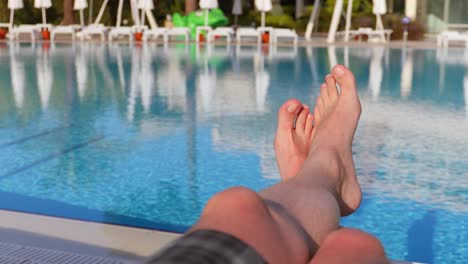 Men's-feet-on-the-background-of-the-swimming-pool,-relax-on-vacation