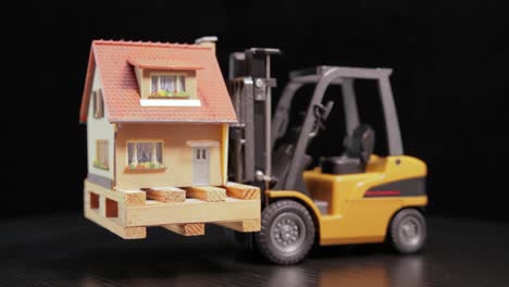 Forklift-truck-holds-a-house-on-a-pallet.-The-concept-of-cargo-transportation-and-logistics,-construction-of-houses-and-buildings.