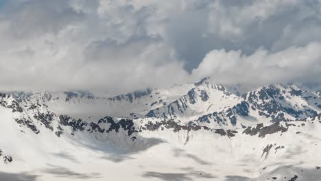 Air-flight-through-mountain-clouds-over-beautiful-snow-capped-peaks-of-mountains-and-glaciers.